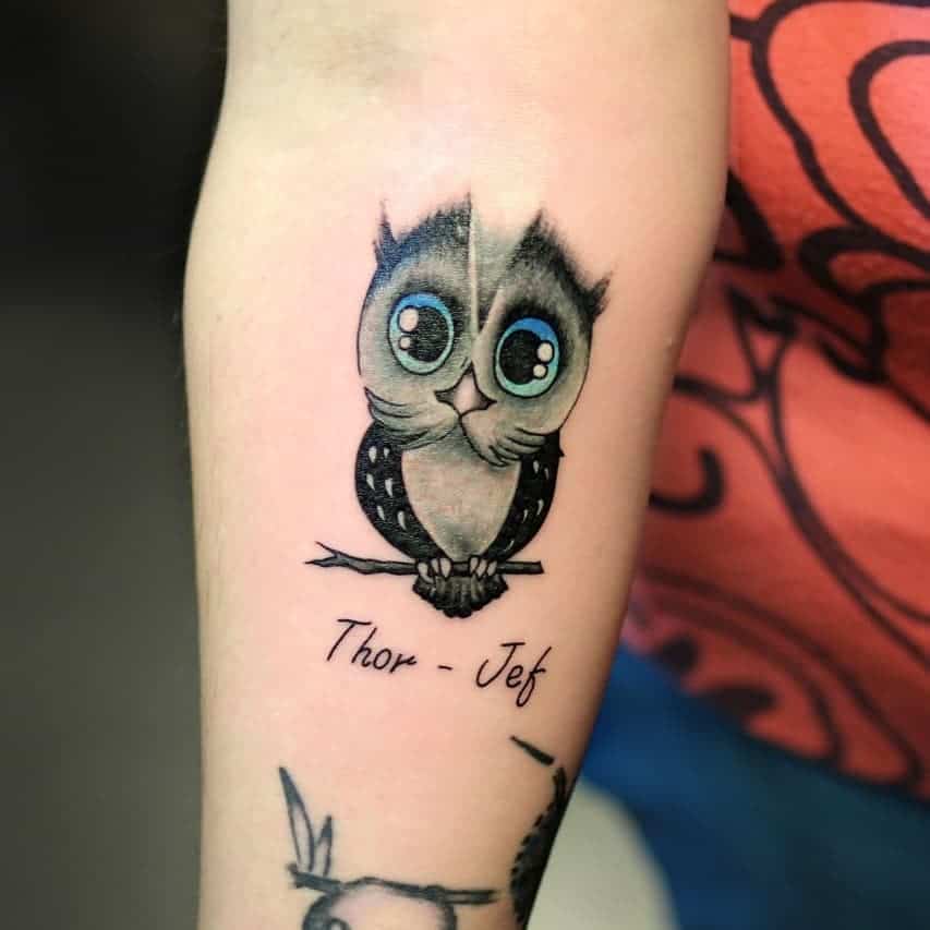 Tattoo van een schattig klein uiltje op een onderam. In black and grey met blauwe ogen, met namen eronder. Geplaatst bij Inksane tattoo en piercing.