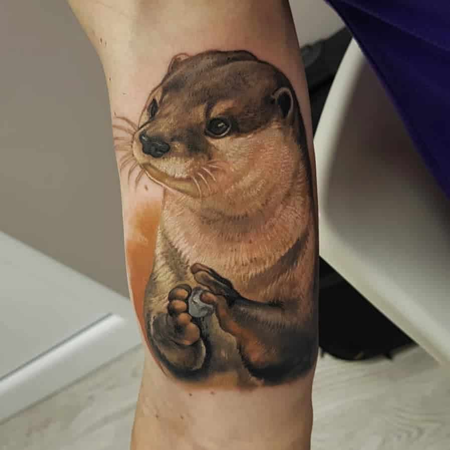 Tattoo van een otter die een steentje vast heeft in kleur realisme. Geplaatst op een onderarm bij Inksane tattoo en piercing.