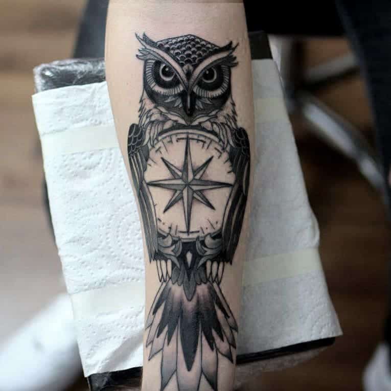 Black and grey tattoo van een uil met kompas op onderarm. Geplaatst bij Inksane tattoo en piercing.