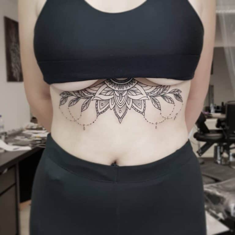 Underboob tattoo geplaatst bij Inksane tattoo en piercing. Mandala met blaadjes en kettingen
